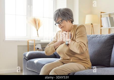 Ältere Frau mit Brustschmerzen, Herzinfarktsymptomen, auf Sofa sitzend Stockfoto