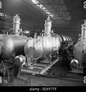 Vintage-Schwarz-weiß-Foto, das zwei engagierte männliche Fabrikarbeiter zeigt, die in den 1960er Jahren neu zusammengebaute große Industrietanks aus Metall im Stroymash-Werk in Sloviansk sorgfältig inspizierten Ein Mitarbeiter überprüft das obere Ventil, während der andere den Elektromotor an der Basis untersucht. Dieses authentische historische Archivbild zeigt den sowjetischen Schwermaschinenbau, komplexe Fertigungsprozesse, qualifizierte Handarbeit und spiegelt den produktiven Alltag eines friedlichen Donbas vor dem Krieg wider. Stockfoto