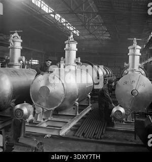 Vintage-Schwarz-weiß-Foto, das zwei engagierte männliche Fabrikarbeiter zeigt, die in den 1960er Jahren neu zusammengebaute große Industrietanks aus Metall im Stroymash-Werk in Sloviansk sorgfältig inspizierten Ein Mitarbeiter überprüft das obere Ventil, während der andere den Elektromotor an der Basis untersucht. Dieses authentische historische Archivbild zeigt den sowjetischen Schwermaschinenbau, komplexe Fertigungsprozesse, qualifizierte Handarbeit und spiegelt den produktiven Alltag eines friedlichen Donbas vor dem Krieg wider. Stockfoto