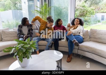 Im modernen Wohnzimmer mit Marmortisch unterhalten sich verschiedene Freunde auf dem geschwungenen beigefarbenen Sofa Stockfoto