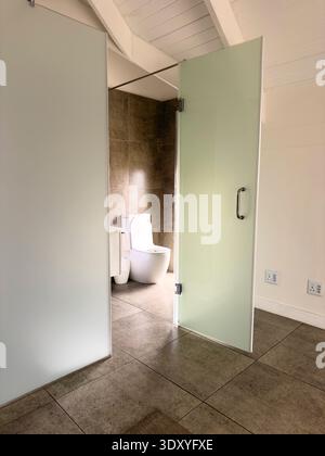 Langebaan Südafrika. 08.02.2025, modernes Badezimmer mit Milchglaspaneelen, freiliegenden Deckenbalken und strukturierten Fliesen Stockfoto