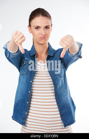 Porträt, wütend und Frau im Studio, Daumen nach unten und schlechte Bewertung auf weißem Hintergrund. Geste, Symbol und Person mit Stress, Frustration und Symbol für Stockfoto