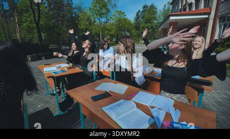 Glückliche Schüler an den Schreibtischen im Freien heben ihre Hände, um das Ende des Schultages zu feiern Stockfoto