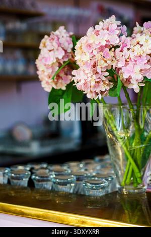 Frische Hortensie-Blüten in klarer Vase mit verschwommenem Café-Hintergrund. Blumendekor, romantische Inneneinrichtung und Veranstaltungsdekoration. Plastikblumen Stockfoto