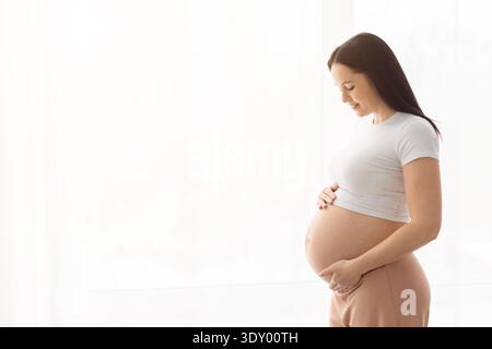Seitenansicht einer jungen schwangeren Frau mit Bauch in hellem Wohnraum Stockfoto