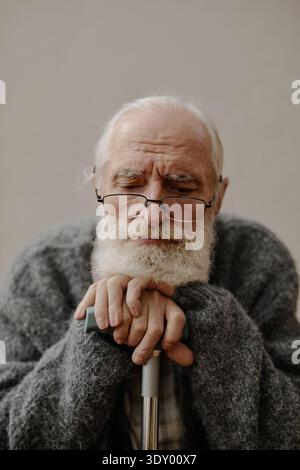 Porträt eines älteren kaukasischen Mannes, der Hände auf Stock legt, während er drinnen sitzt Stockfoto