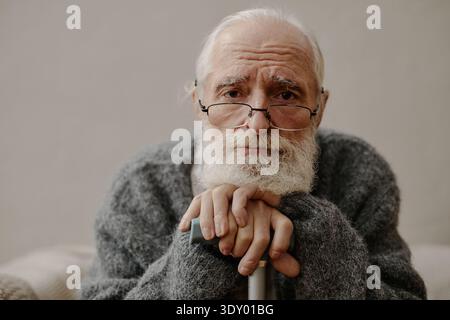 Porträt eines älteren kaukasischen Mannes, der eine Brille trägt, die Hände auf Gehstock ruht Stockfoto