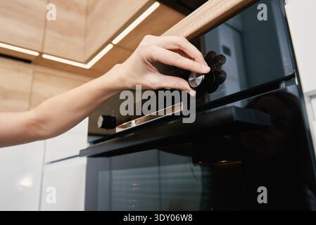 Weibliche Hand wählen Backprogramm auf elektrischen Ofen Bedienfeld, Frau mit elektrischen Ofen, moderne Haushaltsgeräte Stockfoto