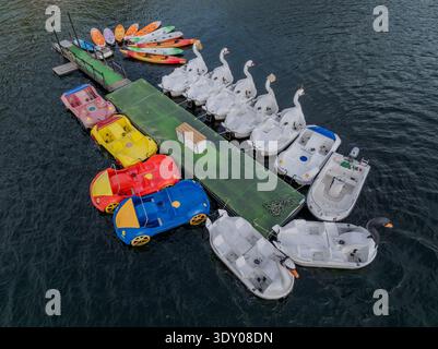 Aus der Vogelperspektive einer lebhaften Sammlung von Schwan-Tretbooten und farbenfrohen Kajaks, die sich um ein Dock gruppieren, im Kontrast zum tiefblauen Wasser, Alqueirão, Stockfoto