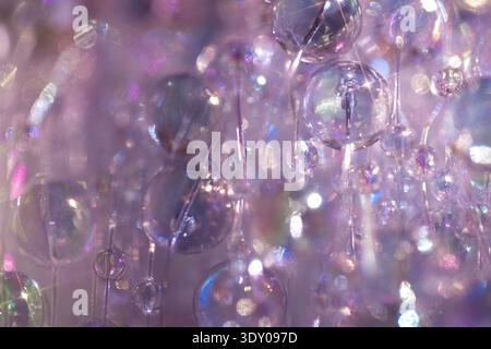 Nahaufnahme von Glasperlen in verschiedenen Größen, die Licht vor einem weichen violetten Hintergrund reflektieren und einen optisch fesselnden Effekt erzeugen Stockfoto