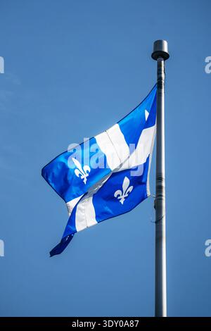 Die Provinzflagge von Quebec mit Fleur-de-Lis-Symbolen, die auf einem Metallfahnenmast vor dem klaren blauen Himmel von unten aus fliegen Stockfoto
