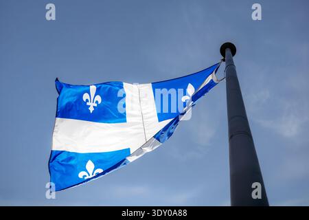 Die Provinzflagge von Quebec mit Fleur-de-Lis-Symbolen, die auf einem Metallfahnenmast vor dem klaren blauen Himmel von unten aus fliegen Stockfoto
