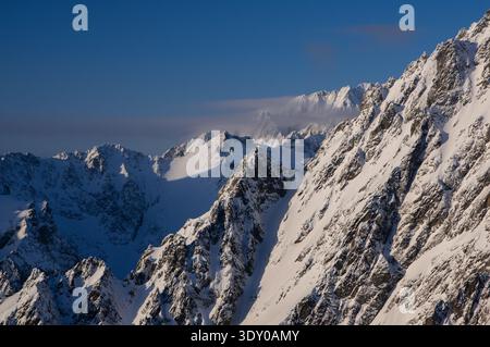 Aus der Vogelperspektive schneebedeckte Gipfel, die durch den klaren, klaren Himmel durchdringen, deren zerklüftete Kanten durch weiße Schwankungen weicher werden, Vysoke Tatry, Presovsky kraj, Slowakei. Stockfoto