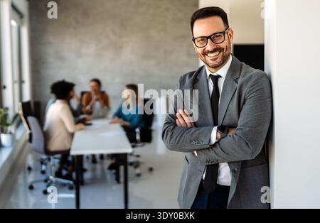 Gutaussehender junger Geschäftsmann, der vor seinem Team selbstbewusst im Firmenbüro steht Stockfoto