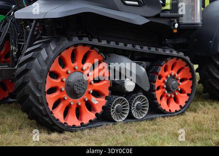 Nahaufnahme von HD-Raupenrädern bei modernen landwirtschaftlichen Traktoren, Gummiraupensystem und großen roten Rollen auf dem Grasfeld Stockfoto