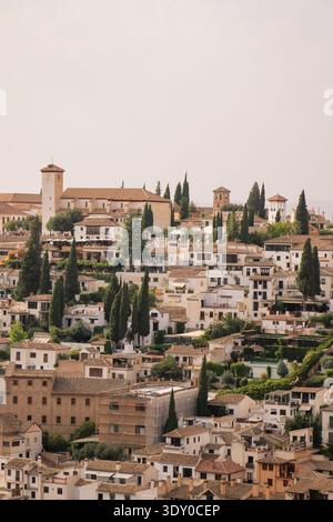 Aus der Vogelperspektive auf die weißen Gebäude des sonnenverwöhnten Viertels Albaicín, gekrönt von den alten Mauern und Türmen der Alhambra, Granada, Andalusien, Spanien. Stockfoto