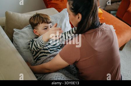 Liebevolle Mutter tröstet ihren kranken Sohn, der sich schlecht zu Hause fühlt Stockfoto