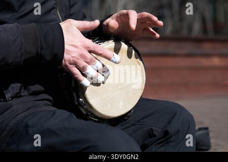 Eine Nahaufnahme der Hände eines Mannes, die eine traditionelle afrikanische Djembe-Trommel spielen. Der Musiker hat ein weißes Schutzband an seinen Fingern. Stockfoto