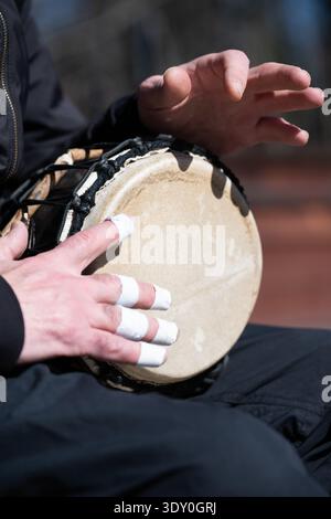 Nahaufnahme eines Musikers, der draußen eine Djembe-Trommel spielt. Hände eines Schlagzeugers mit aufgeklebten Fingern, die ein ethnisches Schlaginstrument spielen. Stockfoto