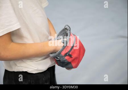 Eine detaillierte Aufnahme einer Kinderhand, die nach weißem Magnesiumpulver in einem rot-grauen Kreidebeutel aus Stoff greift. Unverzichtbare Ausrüstung zum Klettern und Stockfoto