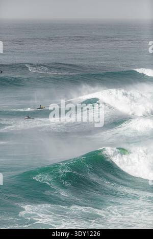 Surfer können sich anmutig durch die mächtigen Meereswellen bewegen. Schaumige Wappen schlagen gegen das tiefgrüne Meer. Ferne Figuren reiten mit fokussierter Entschlossenheit auf Wellen Stockfoto