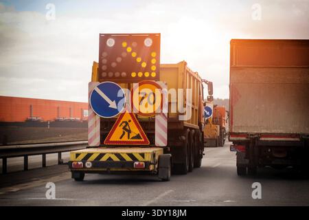 Straßenwartungsfahrzeug hinten. Die beleuchtete Pfeiltafel weist auf Rechtsverkehr hin. Schild „Work Ahead“, Geschwindigkeitsbegrenzung 70, vorgeschriebene Blinkzeichen rechts. Andere Lkws, Stockfoto