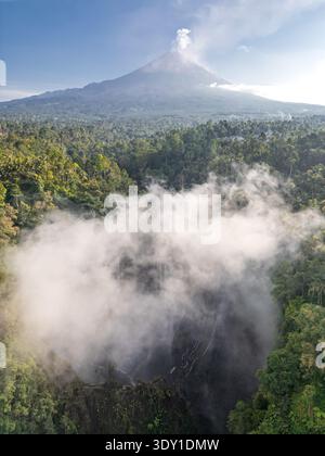 Blick aus der Vogelperspektive auf den Tumpak Sewu Wasserfall bei Sonnenaufgang mit dem Mount Semeru im Hintergrund. Stockfoto