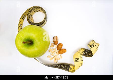 Konzeptuelles Bild für einen gesunden Lebensstil mit grünem Apfel, Mandeln, Hafer und einem Maßband auf weißem Hintergrund. Stockfoto