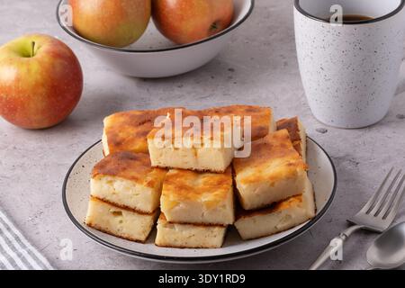 Frisch gebackene Apfelkuchen auf einem Teller mit Äpfeln in einer Schüssel an einem Küchentisch während Stockfoto