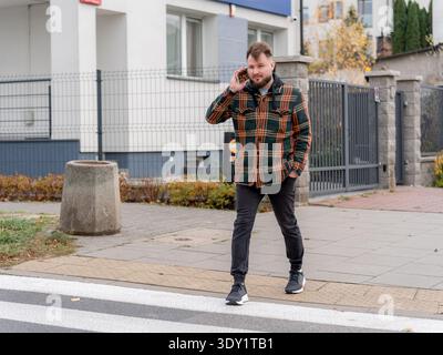 Junger bärtiger Mann, der auf dem Smartphone spricht, während er die Straße entlang läuft. Mobile Kommunikation, Business Call und urbanes Lifestyle-Konzept. Stockfoto
