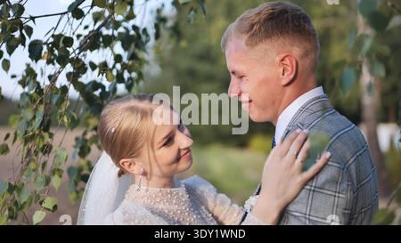 Frisch vermähltes Paar teilt einen zarten Moment unter einer Birke, symbolisiert Liebe und Neuanfang an ihrem Hochzeitstag Stockfoto