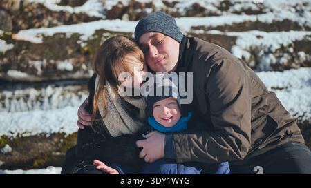 Liebevolle Familie, die sich eng umarmt, warme Zuneigung in der verschneiten Winterlandschaft mit weißer Umgebung teilt Stockfoto
