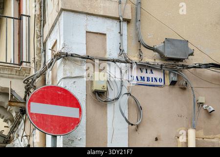 Drähte, Kabel, Abzweigdosen und Straßenschilder an einem Gebäude in der Via Bambino in Catania, Sizilien, Italien. Stockfoto