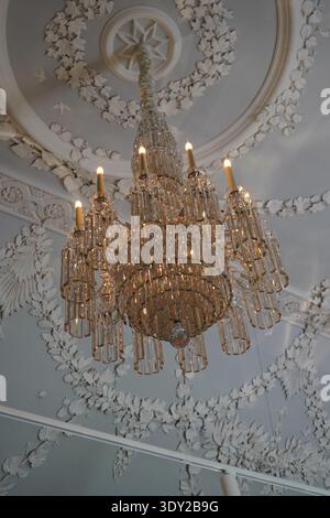 Kunstvoller Kristalllüster, der an einer dekorativen Decke mit detaillierten Stuckarbeiten und warmen leuchtenden Lichtern hängt. Stockfoto