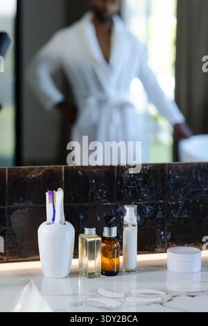 Zahnbürsten und Hautpflegepumpen sitzen auf einer Marmorplatte, nahe dunkler Fliesen. Badezimmer, Spiegel, Reflexion, Kosmetik, Pflege, Stockfoto