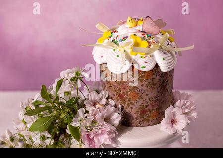 Traditionelles osterkulich mit weißer Glasur, bunten Streuseln und dekorativen Küken, Häschen und Schmetterlingen, mit zarter Kirschblüte arrangiert Stockfoto