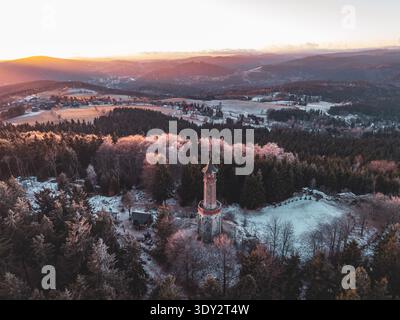 Der Stepanka-Aussichtsturm steht im Winter im Isergebirge hoch. Der Sonnenuntergang wirft warmes Licht über die verschneite Landschaft und den umliegenden Wald. Der Turm bietet einen Blick auf die umliegenden Bereiche. Stockfoto
