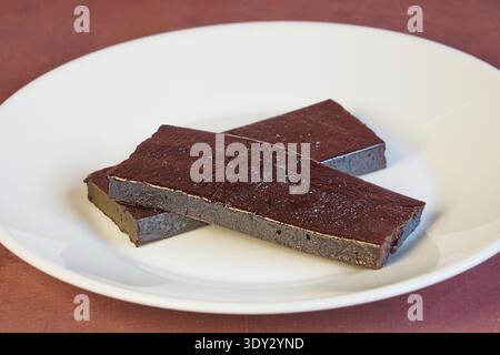 Dunkle Schokoladenriegel auf einer weißen Tafel, belegt mit Kakaopulver Stockfoto
