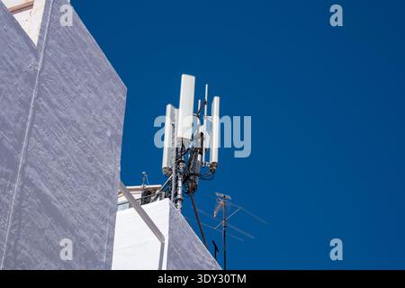 Moderne städtische Kommunikationsinfrastruktur mit Mobilfunkturm gegen klaren blauen Himmel. Stockfoto