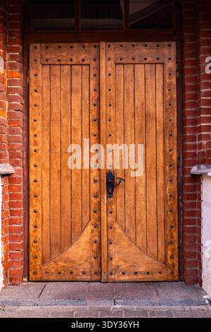 Alte Holztür mit Metallknöpfen und einem antiken Griff in einer Ziegelwand Stockfoto