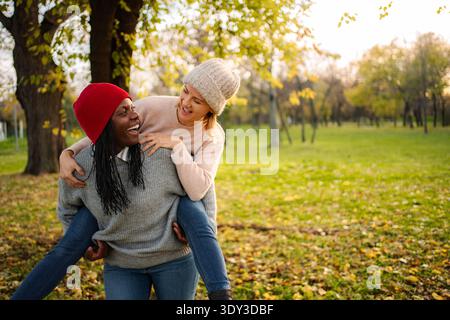 Verschiedene Freundinnen genießen Huckepack-Fahrt im Herbstpark Stockfoto