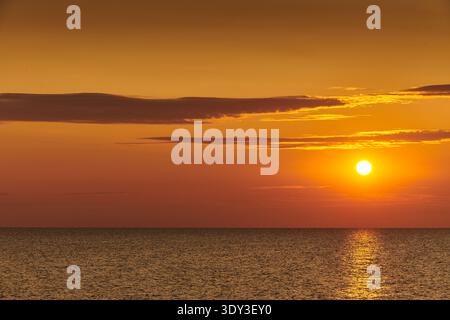 Ein atemberaubender goldener Sonnenuntergang über einem weiten, ruhigen Ozean, bei dem die Sonne tief am Horizont eine brillante Reflexion über das plätschernde Wasser wirft. Die SK Stockfoto