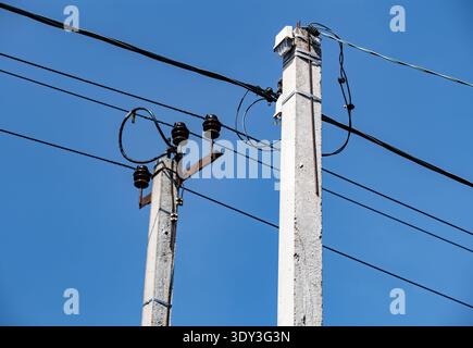 Versorgungsmasten aus Beton, die Stromleitungen gegen einen klaren blauen Himmel stützen Stockfoto