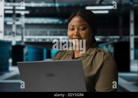 Jolly Programmierer, der Laptop im Rechenzentrum verwendet, um Kennzahlen der Ausrüstung zu verfolgen, die zum Hosten von Websites verwendet wird. Upbeat Server Hub Manager aktualisiert die Kapazität von Speicheranlagen, auf denen Unternehmensdatenbanken ausgeführt werden Stockfoto