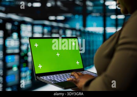 Nahaufnahme des Rechenzentrumsadministrators, der mit einem Green-Screen-Laptop Geräte installiert, die für das Hosting digitaler Dienste verwendet werden. Server-Hub-Mitarbeiter reparieren Mainframes und verwalten Dateiübertragungen mithilfe eines Mockup-Notebooks Stockfoto