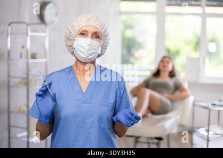 Ältere Ärztin in Maske mit Spritze Stockfoto