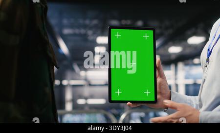 Militärtechniker in Rechenzentren verwenden zur Überwachung von Systemen ein Mockup-Tablet mit grünem Bildschirm. Militärangehörige im Serverraum, die eine stabile Infrastruktur mithilfe eines Chroma Key-Geräts gewährleisten Stockfoto