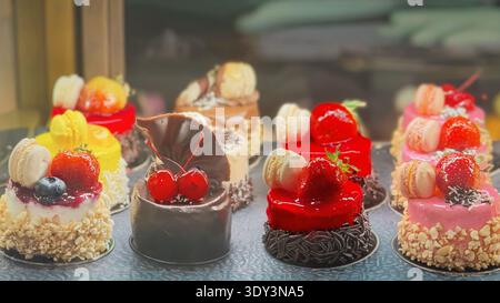Farbenfrohe Miniaturkuchen in der Konditorei, Schaufenster mit Erdbeerbelag, Makronen, Schokoladendekoration. Dessertgebäck, süße Bäckerei Stockfoto