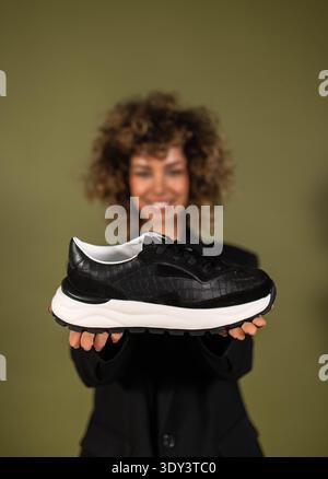 Eine Frau posiert und hält ein Paar Turnschuhe in der Hand Stockfoto