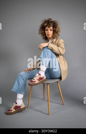 Charmante junge Frau, die auf einem modernen grauen Sessel sitzt Stockfoto